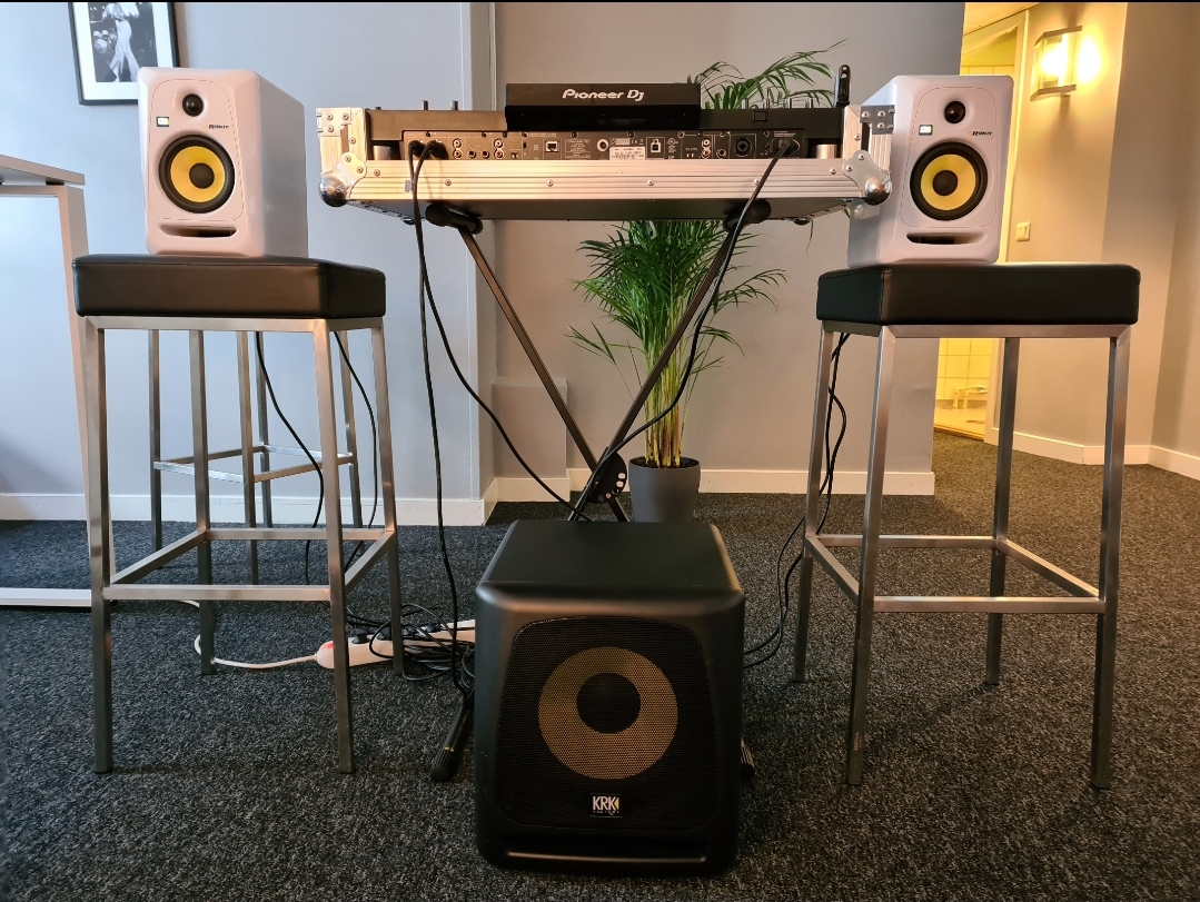 O controlador Pioneer DJ montado num suporte, ladeado por dois monitores de estúdio KRK ROKIT 5 e um subwoofer KRK 10S no Red Panda Studio