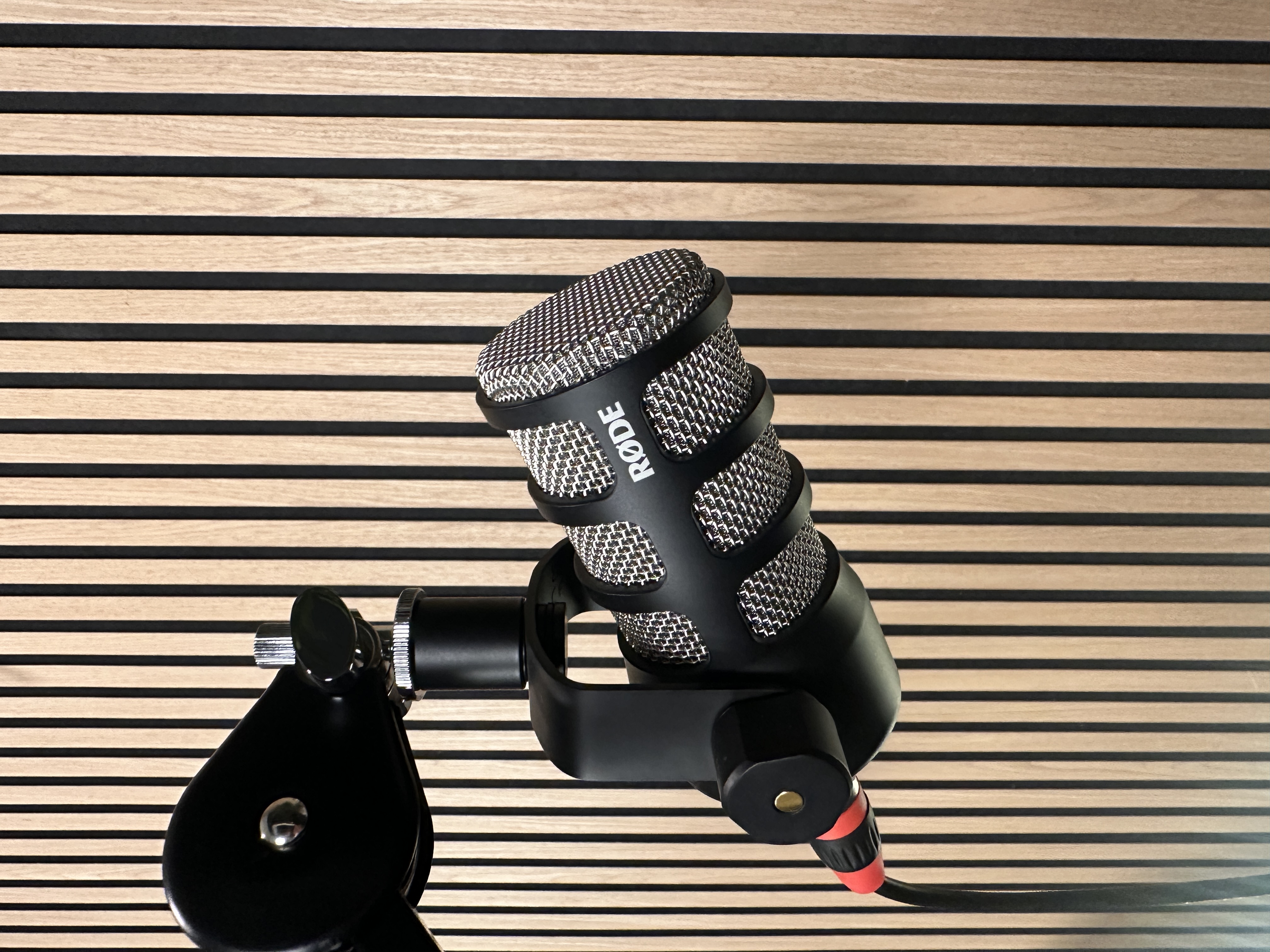 RODE PodMic microphone on a boom arm against the studio's wood slat wall